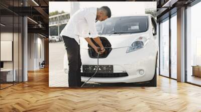 Young Arab man recharging white electric car Wall mural