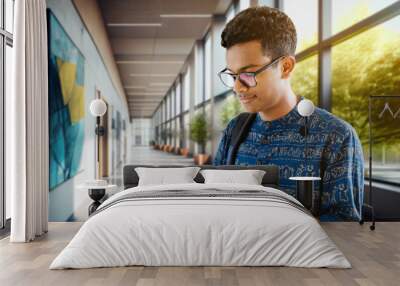 Indian student in the hallway of the university campus looking at the screen of the tablet Wall mural