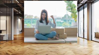 Happy young Asian woman entrepreneur, Smile for sales success after checking order from online shopping store in a laptop at home office, Concept of merchant business online and eCommerce Wall mural