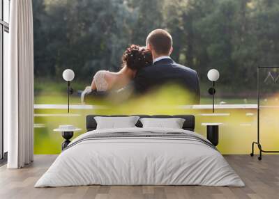 Bride and groom sitting together on bench outdoors. Rear view Wall mural