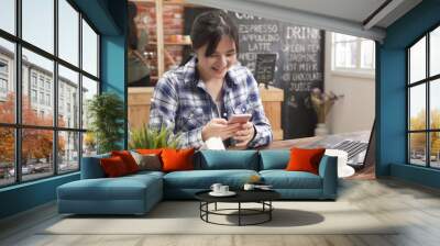 asian business woman in casual wear typing text message on smart phone in cafe bar. young girl freelancer sitting at wooden table with coffee using mobile phone in shop. back view waitress in counter Wall mural