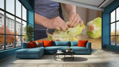 close up female’s hands with finger nail art tearing the lettuce leaf into bite-sized pieces above glass bowl. making fresh vegetable salad. going on healthy diet concept. Wall mural