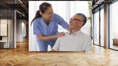 Closeup of caring Asian woman nursing aide talking and encouraging older male patient during home visit. Domiciliary care for elderly senior concept Wall mural