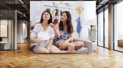 group of mad girls friends sitting on sofa try to turn air conditioner having problem no solution by remote control no battery. young women staring at air cooler up on ceiling in hot summer day home Wall mural