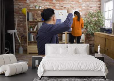 handsome asian male executive sitting at wooden table talking to female coworker employee working by clipboard architect company. happy man leader telling woman colleague good news excited raise hand Wall mural