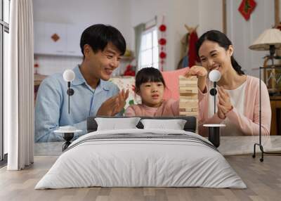 happy asian parents clapping hands and praising their daughter who did good job in playing toy wood blocks while they spending time together on chinese new year at home Wall mural