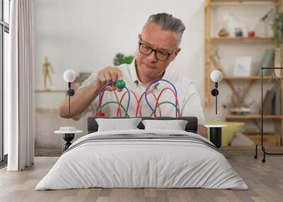 portrait of asian elderly male with tremor practicing exercising hand and wrist using bead maze at home. physical training for Parkinson’s disease in seniors concept Wall mural