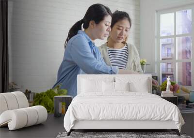 skillful asian chinese woman cooking at home and teaching friend some tips. Home party girl roommates preparing healthy meal for guests. two happy ladies making vegan food on hot pan by window Wall mural