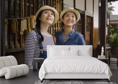 summer holidays vacation happy people concept. group of asian female friends tourists looking up sky while visit japanese wooden temple with wishing wall in background. young girls smiling enjoy view Wall mural