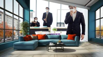 Business men wear mask and cough while business women wearing masks at work to prevent the corona virus outbreak in the background. Wall mural