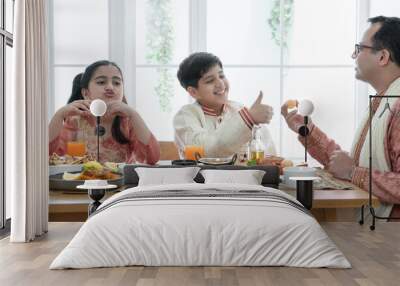 Happy Indian family enjoy eating food with hands, South Asian father and children wear traditional clothes, sitting at dining table at home together. Indian culture lifestyle. Wall mural