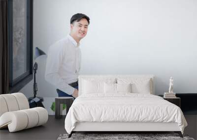 Portrait of Asian young smart handsome businessman wear white shirt holding formal suit in hand sitting on desk smiling at camera. Confident man working with laptop at office. White background Wall mural