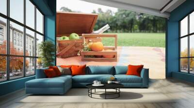 Selective focus on oranges and little flowers in wooden basket and basket of green apples and drinks in glass bottle place on color mat in green park at sunny day. Copy space Wall mural