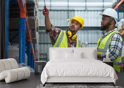 Serious Asian foreman holding walkie talkie and African engineer in safety hat look at inventory, working at site, listing problem on clipboard to discuss, inspect plan for new building at warehouse Wall mural