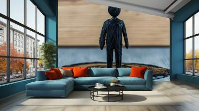 A sculpture of a small, black figure standing on a glossy surface, suggesting themes of isolation and reflection. Wall mural