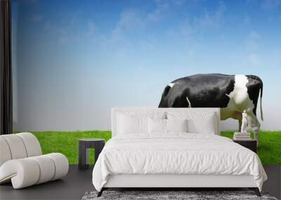 Black and white cow on clean sky and green field eating grass Wall mural