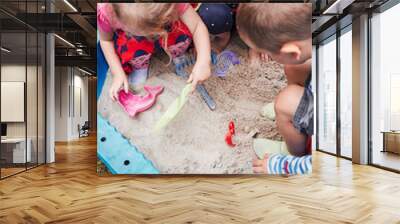 Children, little girls and boy, playing in sandbox in playground outside on summer day. Real people, authentic situations Wall mural