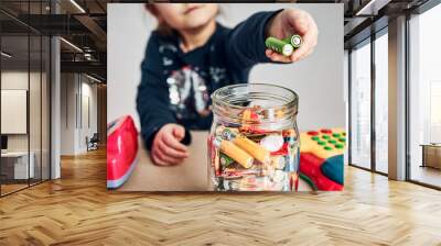 Little girl putting used batteries into jar for recycling. Child separating waste. Batteries only container Wall mural