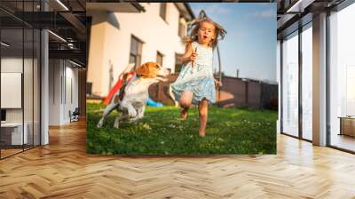 Baby girl running with beagle dog in garden on summer day. Domestic animal with children concept. Wall mural