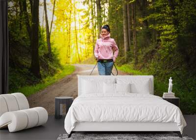 Young woman and dog running together in sunny forest. Wall mural