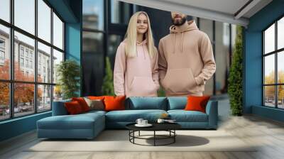 young bearded man and blonde girl is standing in plain hoodie for logo printing. Clothing mockup for hoodie. Autumn youngsters streetwear Wall mural