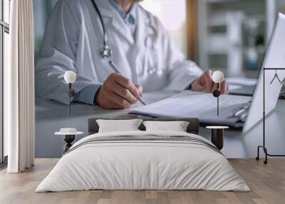 Senior male doctor in white uniform writing notes in notebook, taking notes, working at desk, typing on laptop computer. Wall mural