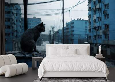 A cat sits on a snowy rooftop and gazes out at the empty, blue city street below. Wall mural