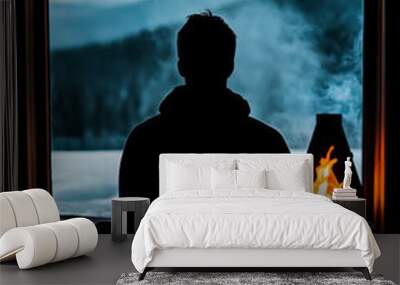 A serene silhouette of a person meditating by a cozy fire, overlooking a breathtaking snow-capped mountain landscape. Wall mural