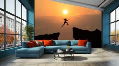 Man jump through the gap between hill.man jumping over cliff on sunset background,Business concept idea Wall mural