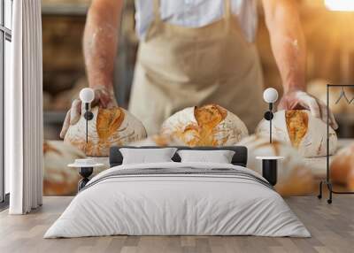 A baker arranging fresh artisanal bread loaves on a wooden table in a bakery with a warm, rustic atmosphere. Wall mural