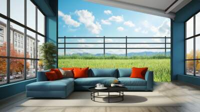 A serene landscape featuring a lush green field under a bright blue sky, complemented by fluffy clouds and a wooden fence. Wall mural