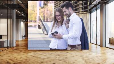 Couple of man and woman in break with coffee to go on hands looking ang the mobile phone Wall mural