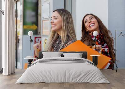 Two woman in shopping with bags on hands in front of window at the street Wall mural