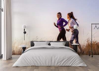 Young and happy best female friends in sportswear jogging together in nature Wall mural