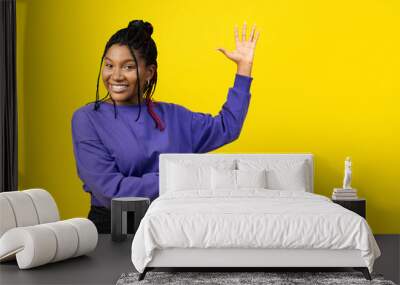 Afro woman presenting something on a vivid yellow background, conveying positivity and enthusiasm. Wall mural