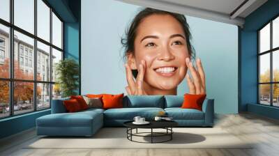 Beauty face. Smiling asian woman touching healthy skin portrait. Beautiful happy girl model with fresh glowing hydrated facial skin and natural makeup on blue background at studio. Skin care concept Wall mural