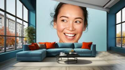 Beauty face. Smiling asian woman with perfect skin portrait. Beautiful happy girl model with healthy glowing facial skin and natural makeup and white smile on blue background at studio Wall mural