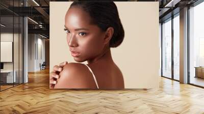 Beauty. Mixed Race Woman Portrait. Beautiful Ethnic Model Touches Her Shoulder And Looking Away. Female With Perfect Glowing Skin And Nude Natural Makeup Posing Against Beige Background. Wall mural