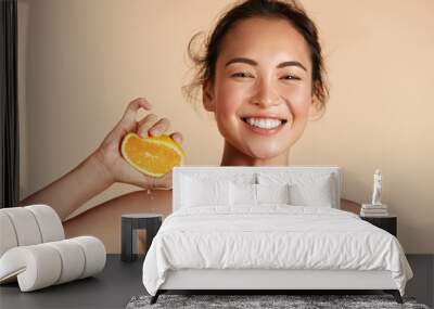 Beauty. Woman with radiant face skin squeezing orange in hand portrait. Beautiful smiling asian girl model with natural makeup, glowing facial skin and citrus fruit. Vitamin C cosmetics concept Wall mural