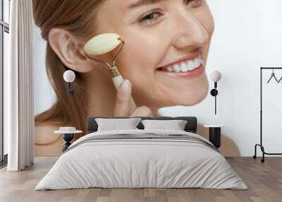 Face massage. Smiling woman using jade roller for skin care Wall mural