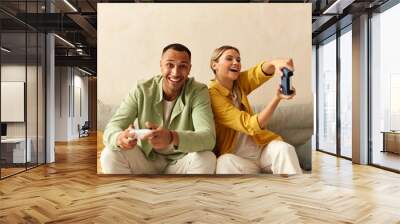 Happy Couple Playing Video Games. Boyfriend And Girlfriend Sitting On Couch In Living Room Enjoying Playing Video Games And Spending Time Together. Enjoying Moment On Weekend Concept Wall mural