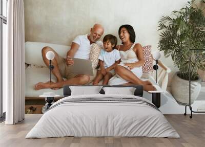 Happy Family On Sofa. Portrait Of Mixed Race Parents With Little Son Using Tablet And Enjoying Leisure On Summer Vacation At Tropical Resort. Different Ethnic Mom And Dad With Boy On Weekend. Wall mural