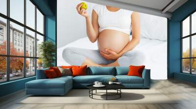 Pregnant Young Woman holding Apple while sitting on the Bed. Hea Wall mural