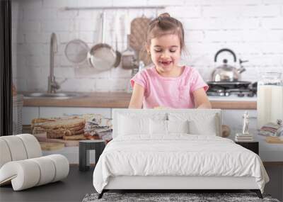 A cute little girl is cooking homemade cakes in the kitchen. Wall mural