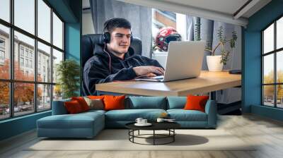 A young male athlete sits in front of a laptop in his room. Wall mural