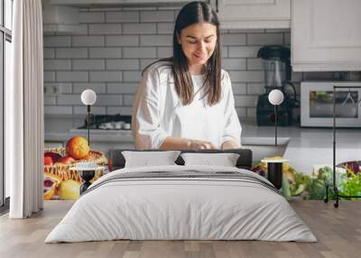 Attractive young woman cutting vegetables for salad in the kitchen. Wall mural