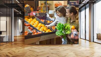 Family in the supermarket. Beautiful young mom and her little daughter smiling and buying food. Wall mural