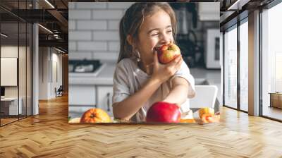 Funny little girl eating apples in the kitchen, health and nutrition concept. Wall mural