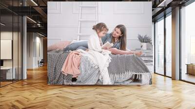 Happy family. Mother and daughter reading a book on the bed. Wall mural