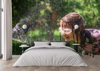 Happy girl splash and plays with garden hose with sprinkler in backyard. Wall mural